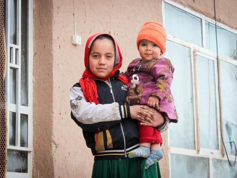 An Afghan girl holds her sibling in her arms