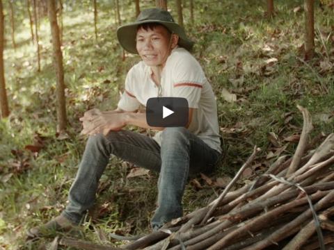 Minh, father who learned to provide for his family in Vietnam through hollistic development approaches, sits in the woods by some firewood