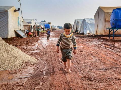 small child walks alone through a refugee camp of tents