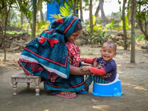 A woman helps her child use a blue plastic toilet