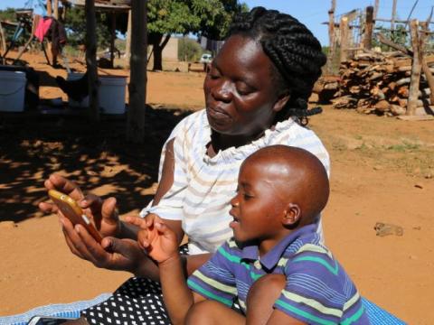 A woman helps a little boy scroll to see something on her phone on a sunny day