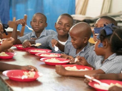 A group of school children eating food from red plates in a lunch room