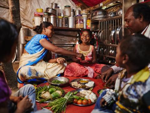 Mother hands food to her daughter as their family eats together