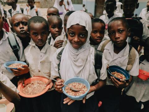 Children gathering with bowls and plates of food in Tanzania, provided by World Vision