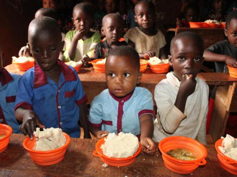 Children gather around a table with bowls of food as part of school meals programming