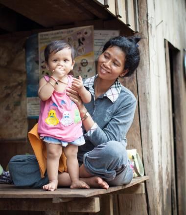 Khmer mother smiles as she holds up her baby toddler so she is standing 