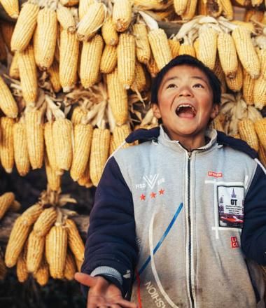 Child in China joyfully standing in front of backdrop of corn