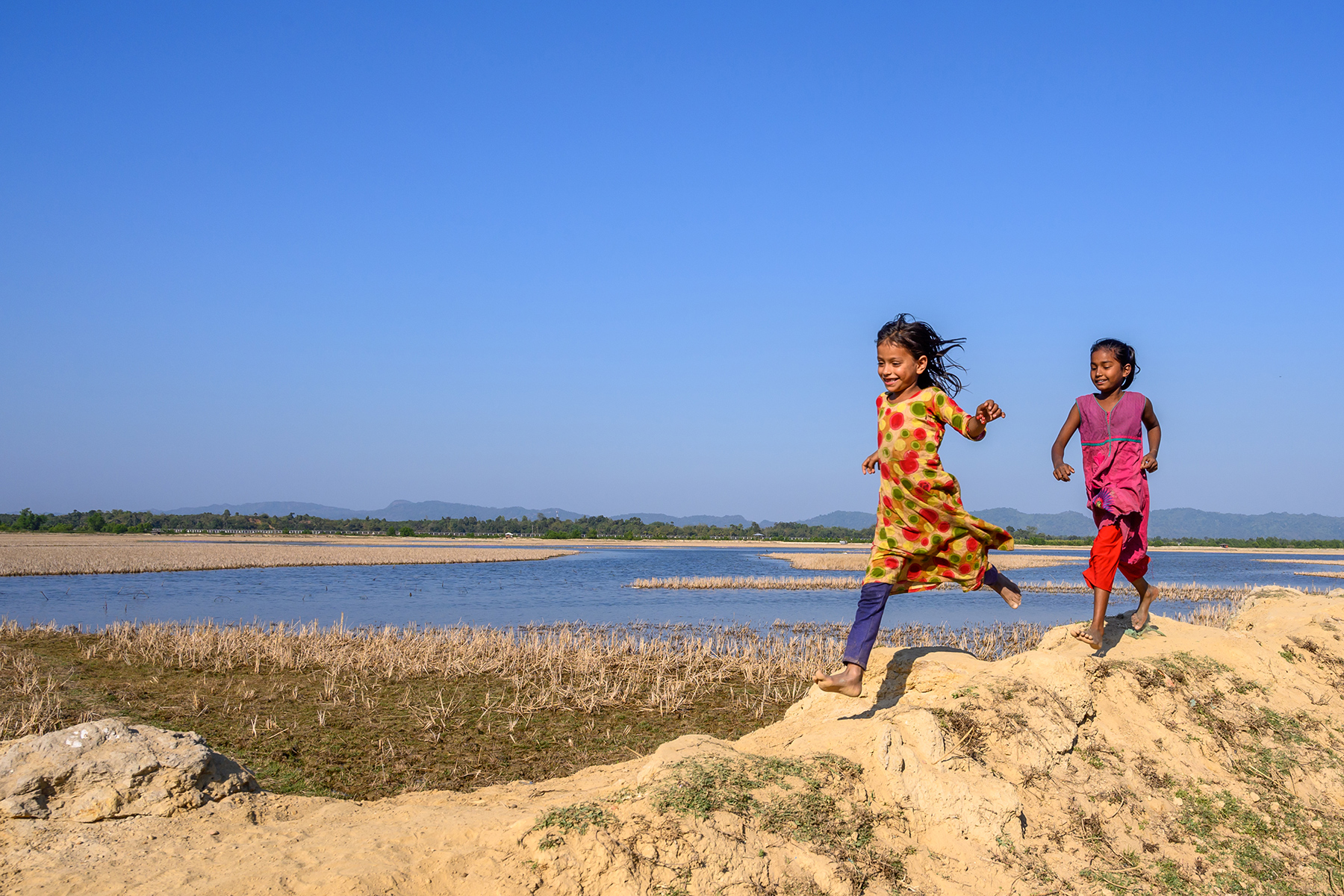 Children run along a lake in Bangladesh