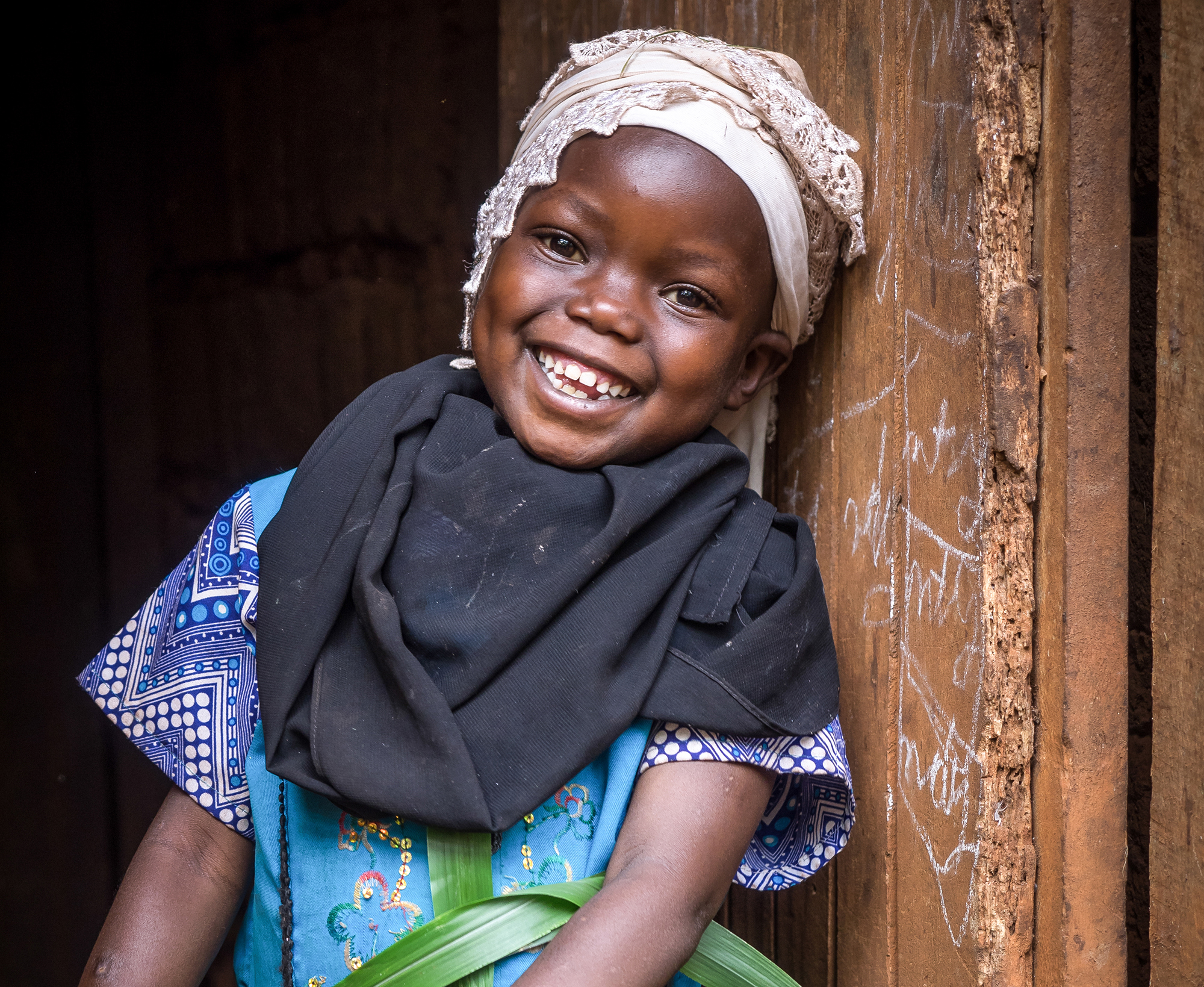 A girl stands against a wall smiling