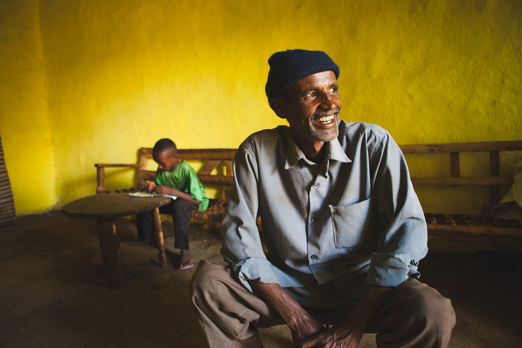 An Ethiopian man in his home with his son reading in the background