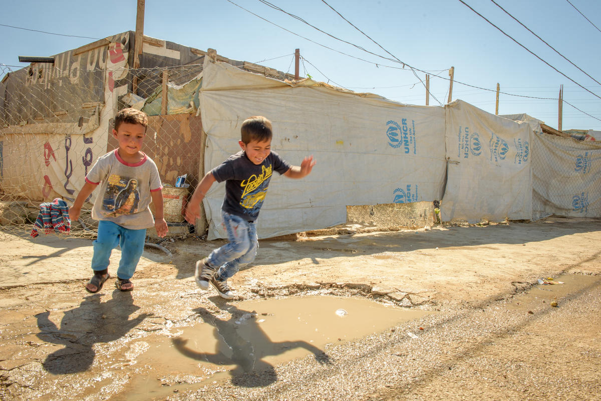Two boys jumping in puddles at refugee camp