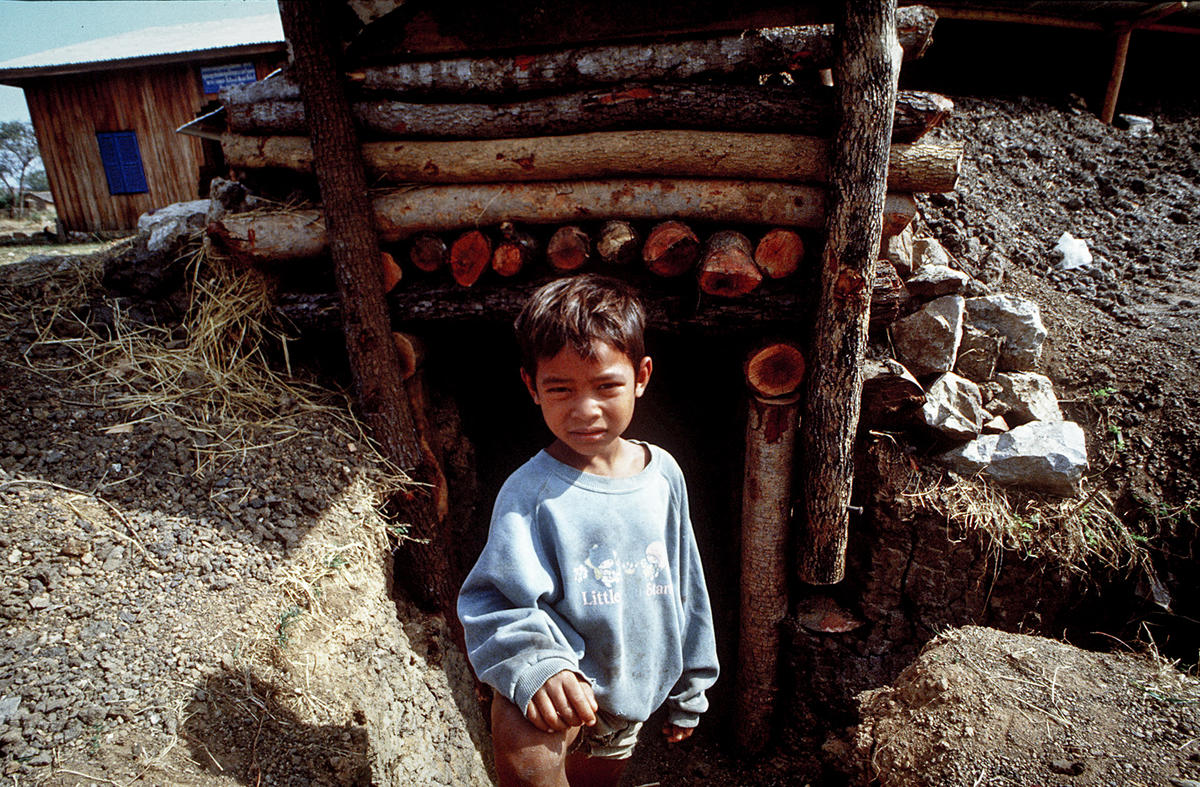 Young Khmer boy stands outside bomb shelter in rural Cambodia province.