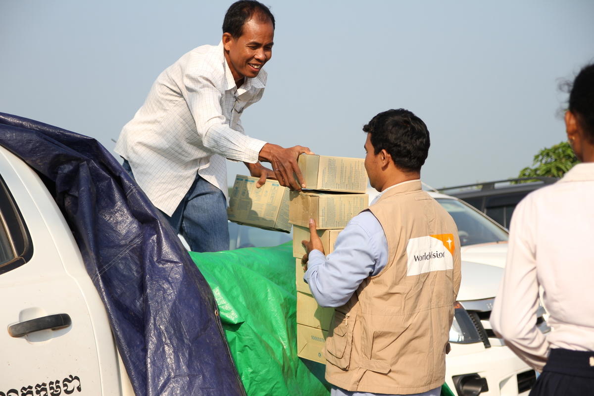 Two men from the World Vision emergency response team unload food supply boxes from the back of a white ute