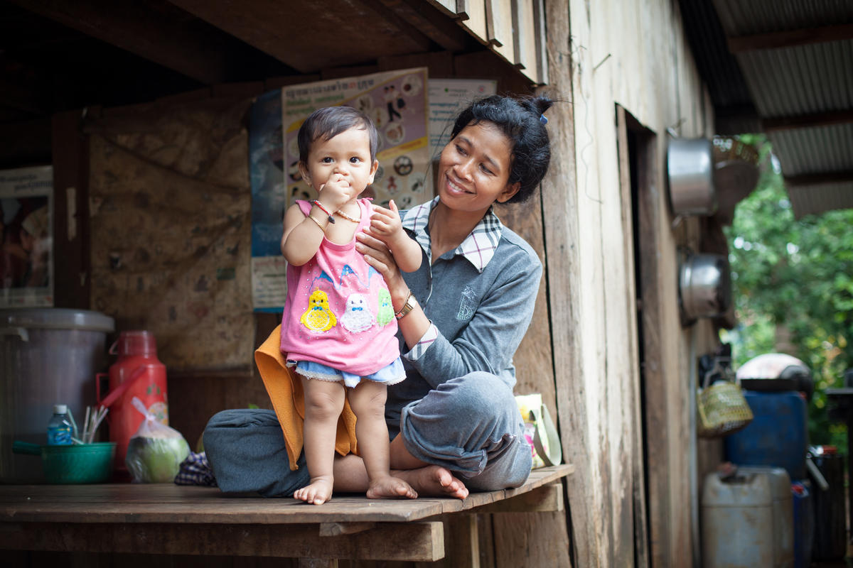 Khmer mother smiles as she holds up her baby toddler so she is standing