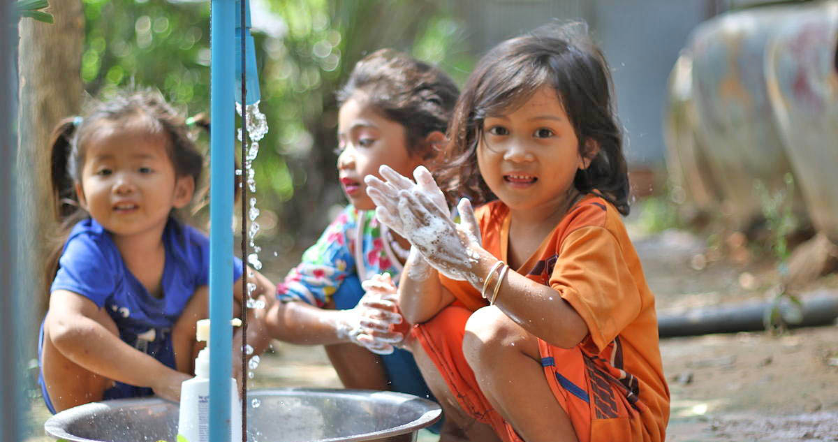 Three Khmer girls wash their hands in a bucket from a tap installed by World Vision Cambodia