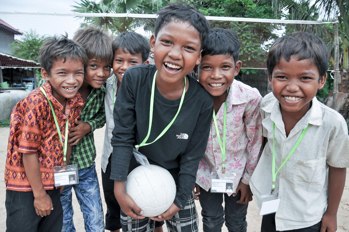 Group of three Khmer boys all smiling and laughing on outdoor volleyball court, Cambodia.