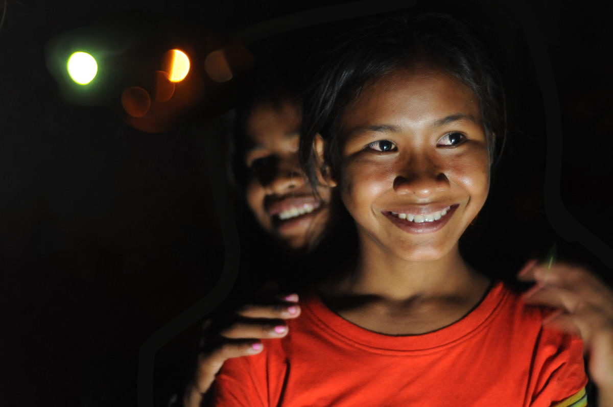 Two young Khmer women stand smiling, it is night time