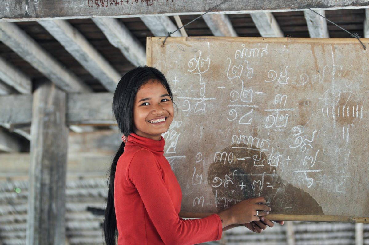 Khmer youth stands in front of blackboard with Khmer script teaching students at youth club, Cambodia