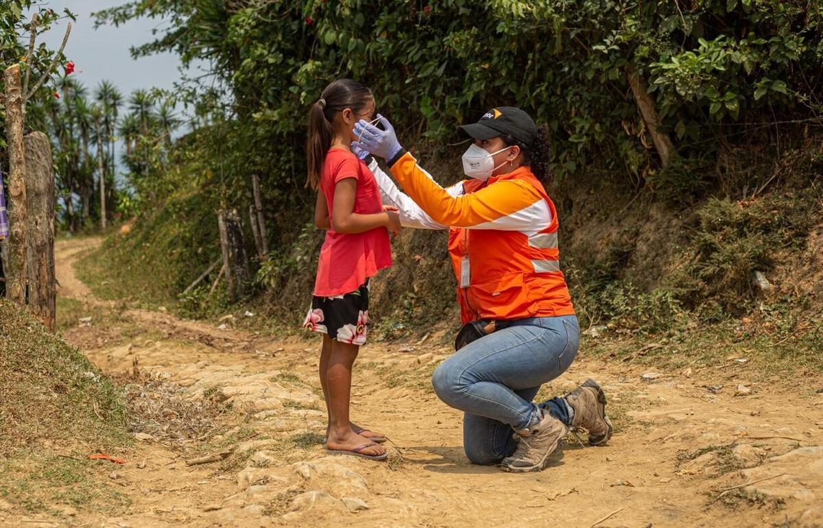 World Vision staff helps child put on mask