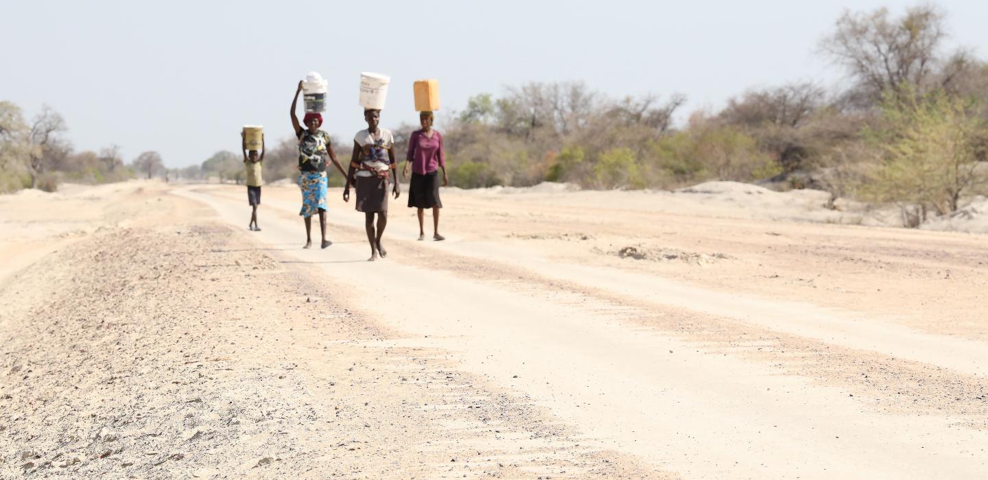Women and girls walk along a dusty road in Angola looking for water
