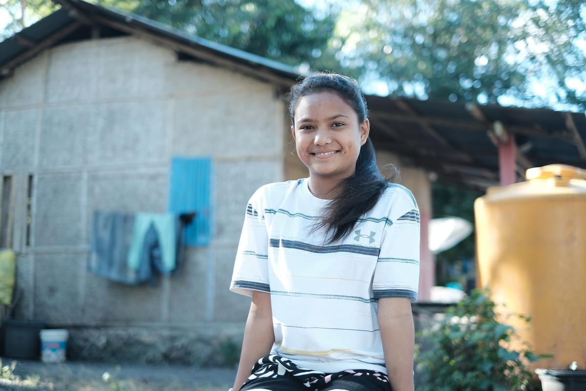girl sits outside a house smiling