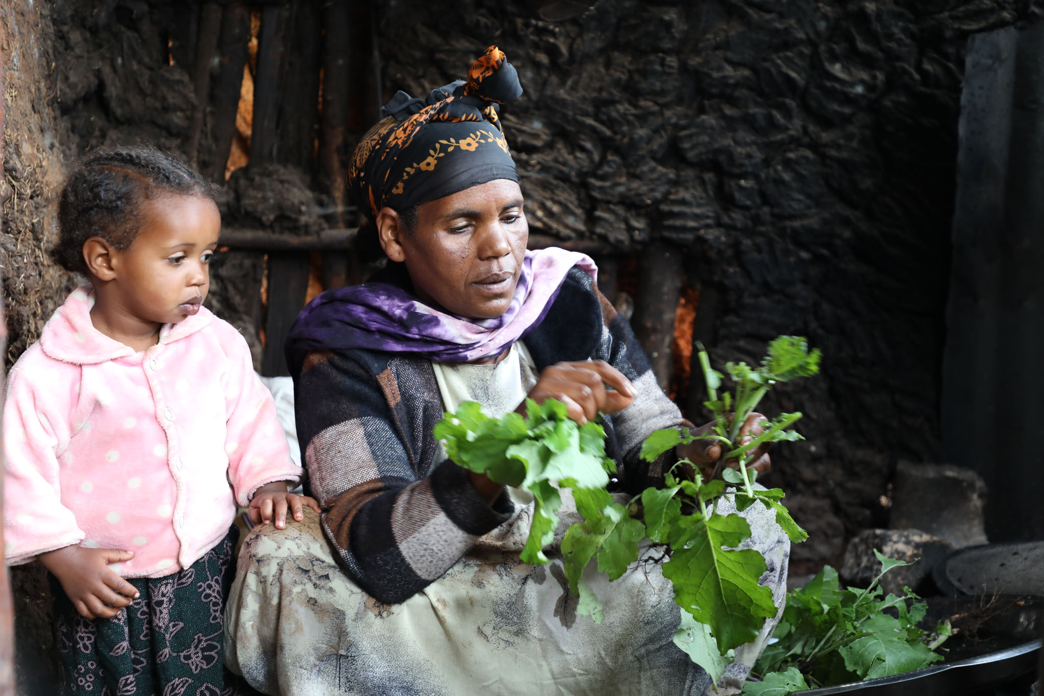Kelemwa preparing Ethiopian kale harvested from her garden, with her two-year-old daughter, Fikir, by her side.