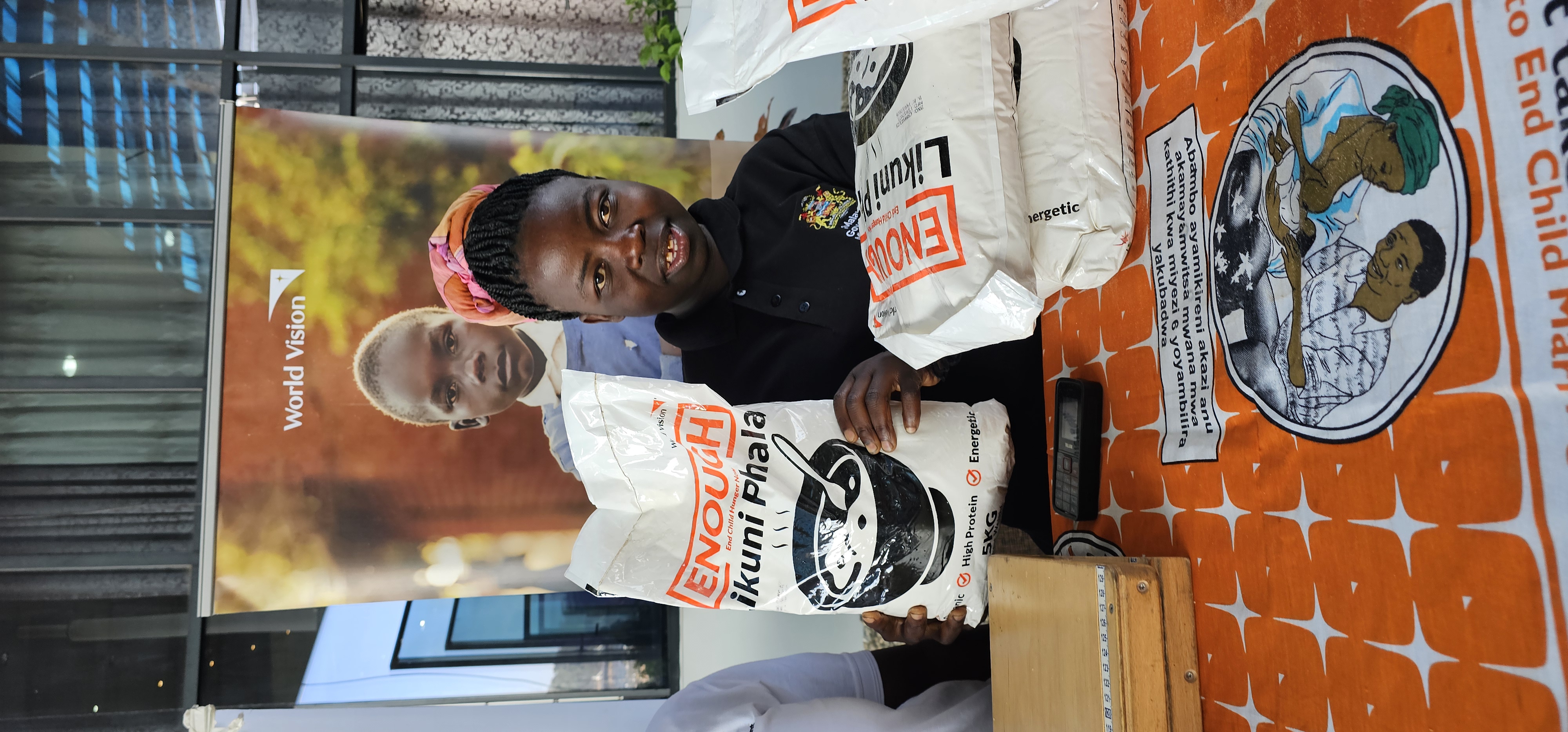 Mercy, Caregiver for Zalare ECD showcasing Corn Soy Blend packet being distributed in WVM Area Programs as part of Enough Campaign School Feeding Program