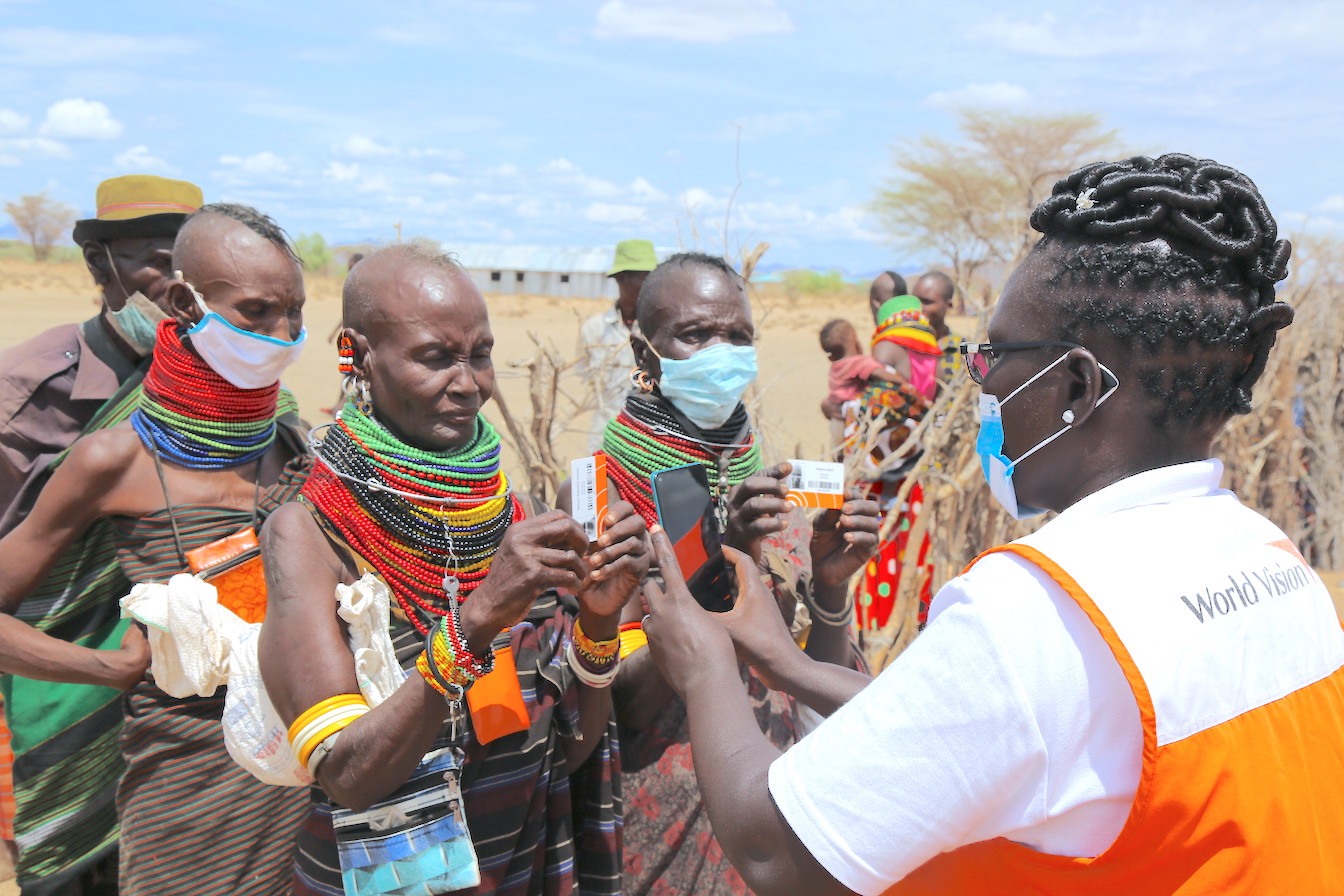 Lilian (a World Vision Emergency specialist) scans beneficiaries' cards using World Vision's innovative Last Mile Mobile Solution (LMMS) technology. The technology helps with the easy identification of targeted beneficiaries, while ensuring that all of them get the right amount of food, based on their needs©World Vision photo/Martin Muluka.