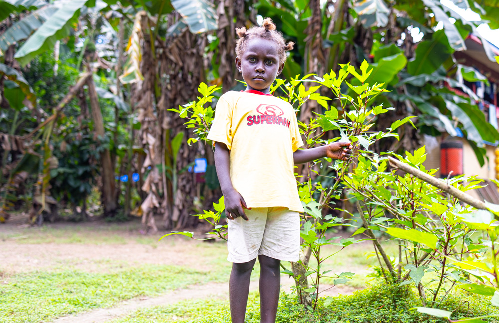 Jamica standing next to the greens at the backyard gardening