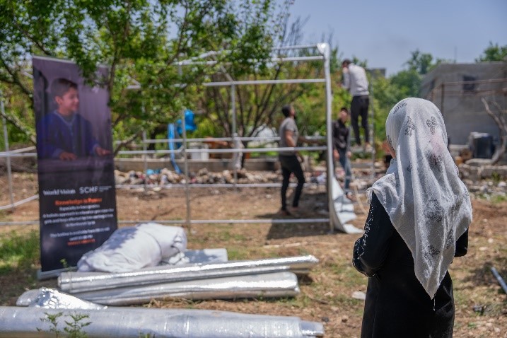 Qamar watching as World Vision Syria Response staff assemble her new tent.