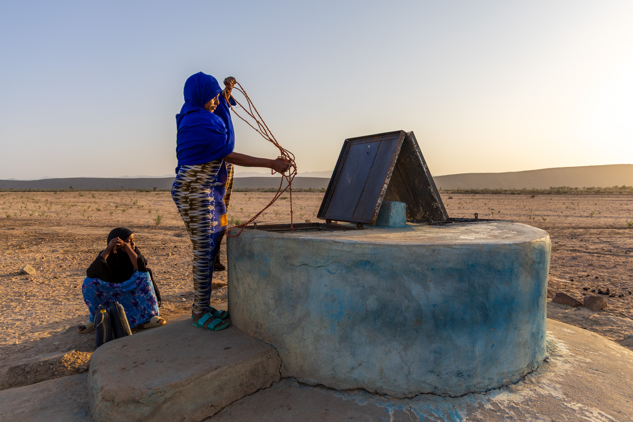 Awo, with her daughter beside her, draws water from an almost dry well. The water level has dropped drastically and is expected to run out within two weeks, leaving the village without any source of water.