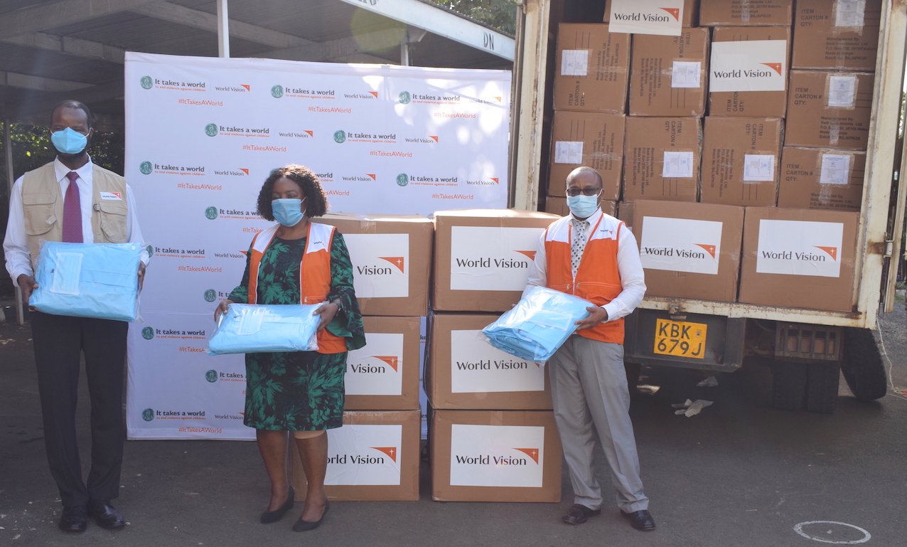 Dr. Stephen Omollo (Vice President for World Vision in East Africa), Lilian Dodzo (National Director for World Vision Kenya) & Gershon Mwakazi (COVID-19 Response Director for World Vision Kenya)holding some of the  Personal Protective Equipment kits donated to Ministry of Health. The kits contain surgical masks, shoe covers, scrub bottoms, aprons and coveralls.©World Vision Photo