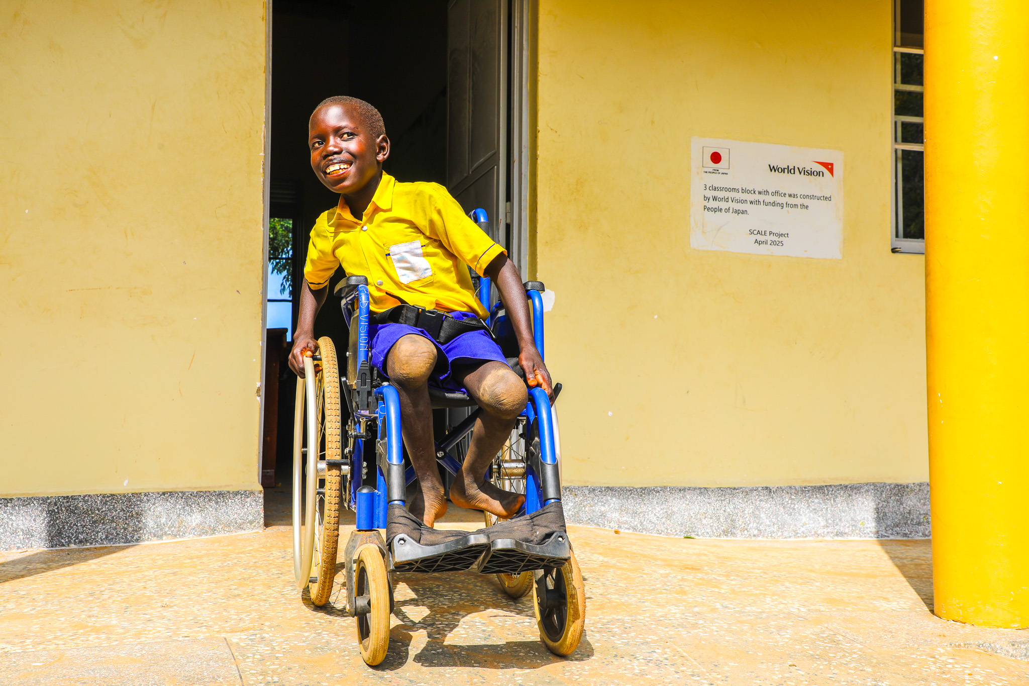 Lematia with his wheel chair at the entrance of the 3 classroom block constructed by World Vision