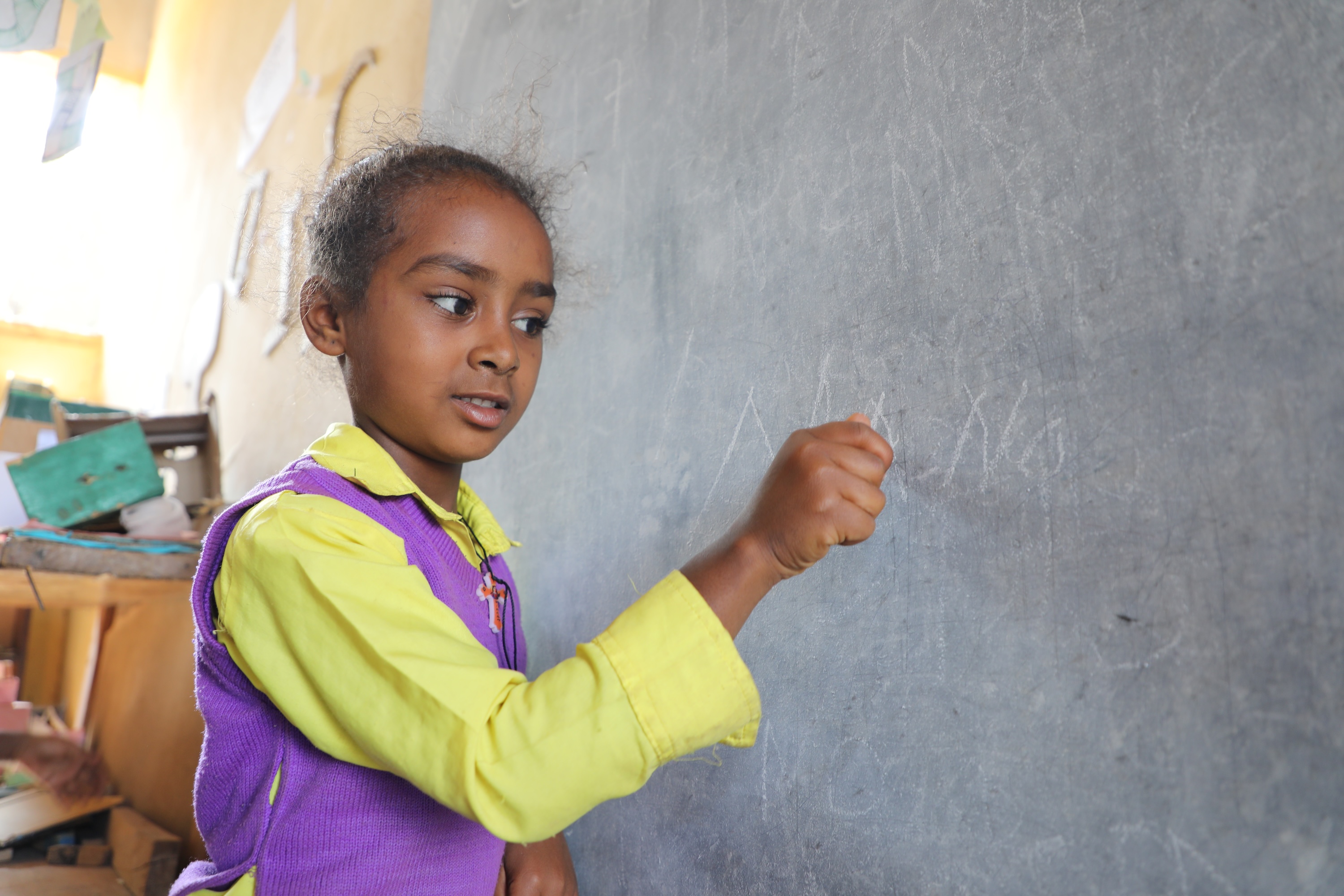 Kalkidan writing with chalk on a classroom blackboard at ECD centre