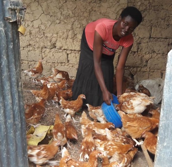 Agnes cheerfully feeding her chicken at her poultry farm