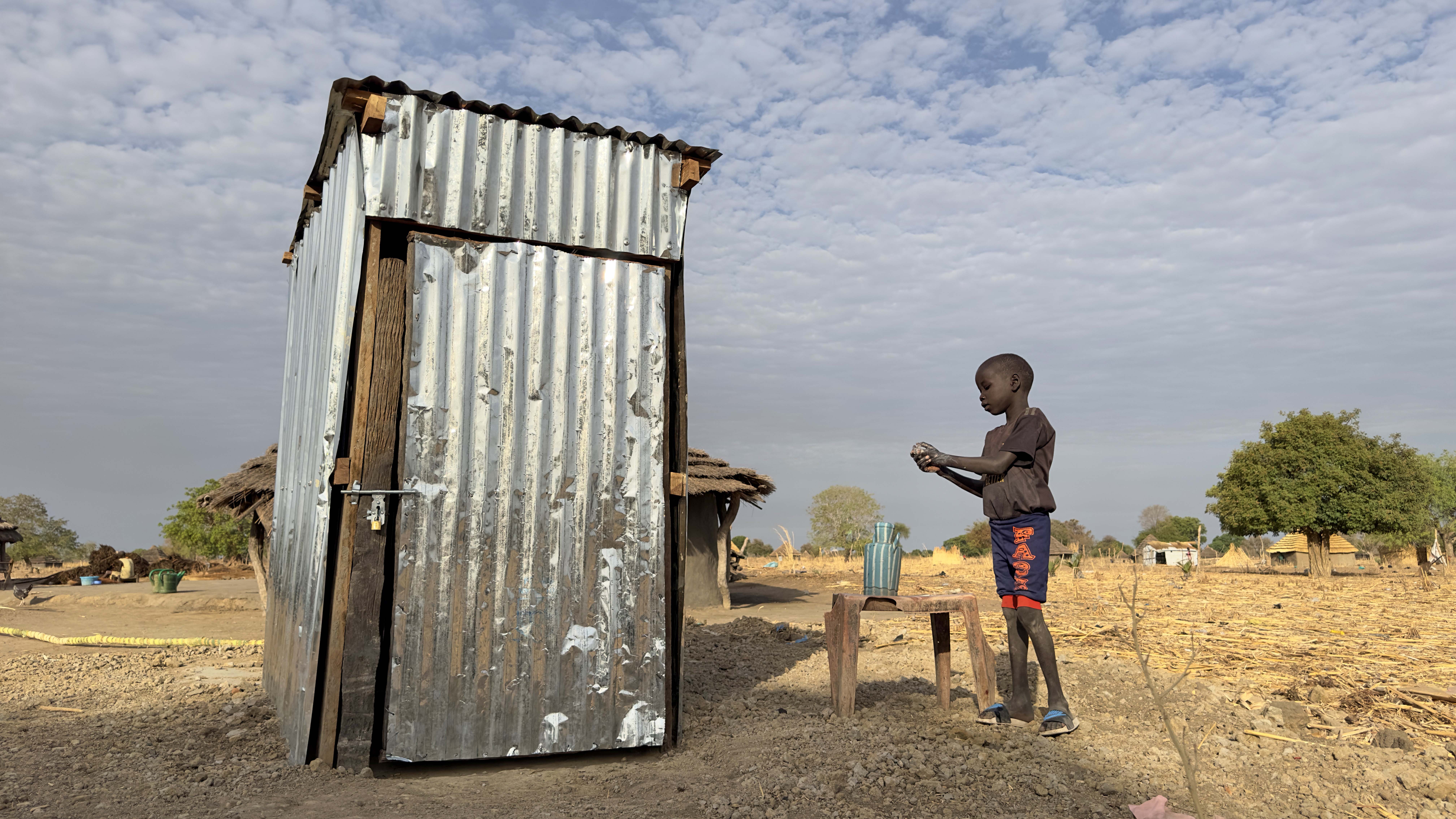 Akur’s 9-year-old son, Deng, washes hand after using the communal emergency pit latrine.