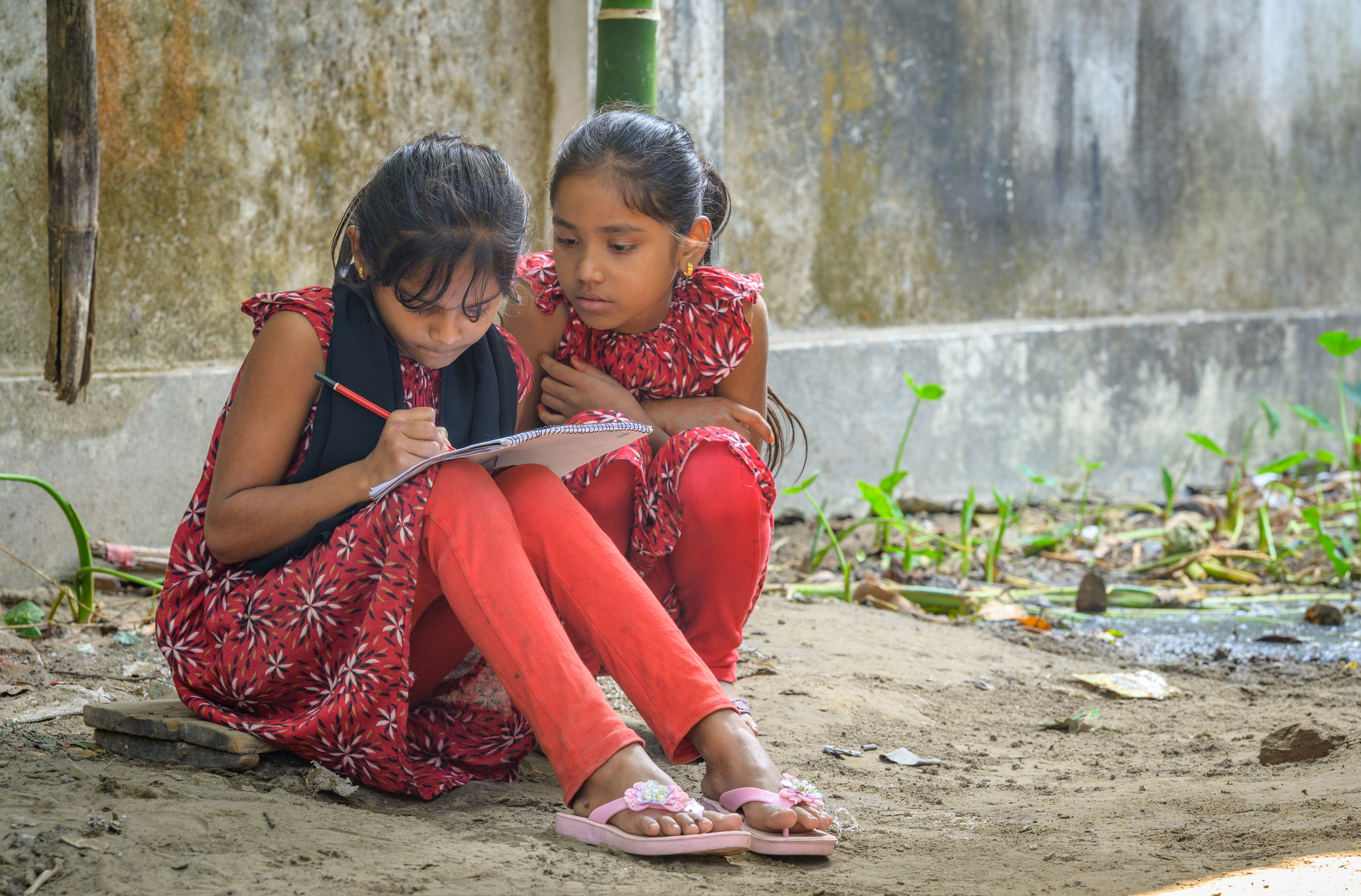 Noor, aged 12, studies while her twin sister Mokarrama looks on. Bangladesh, 2025.