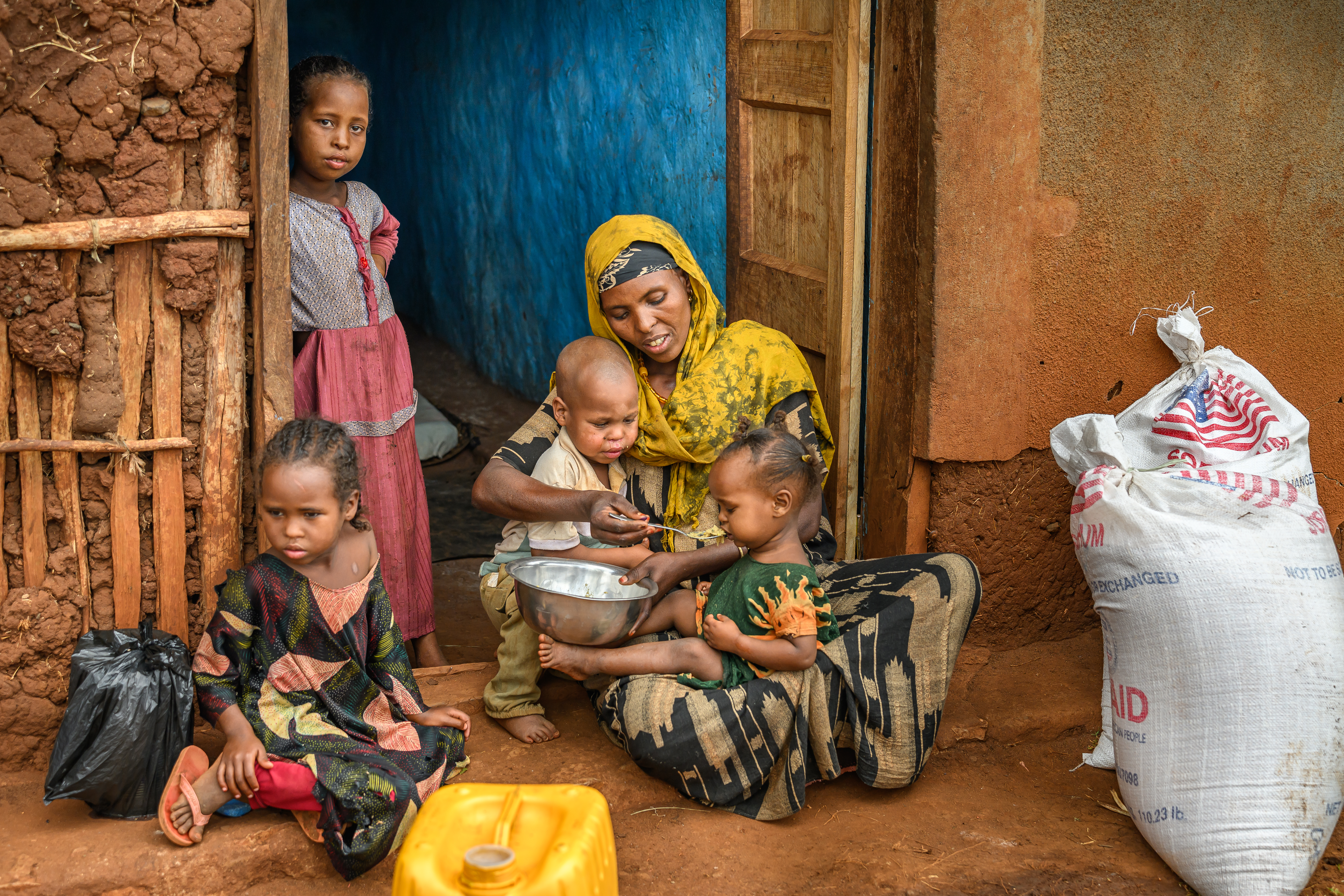 Amina feeds her almost‑two‑year‑old daughter, Mone, while her three other children gather around / Ethiopia / 2025.