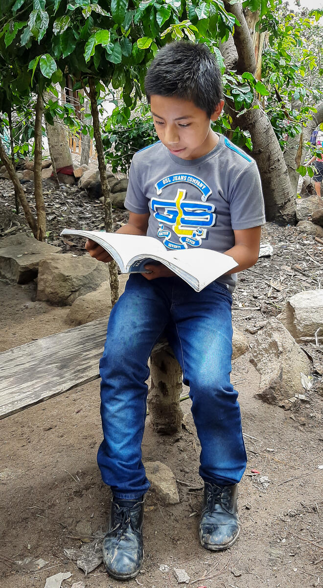 Hector reading  abook outside his home. 