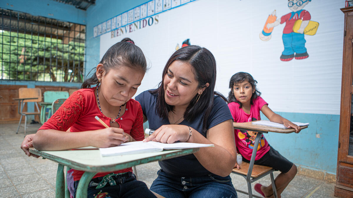 Dassari helps a child in her classroom work on school work