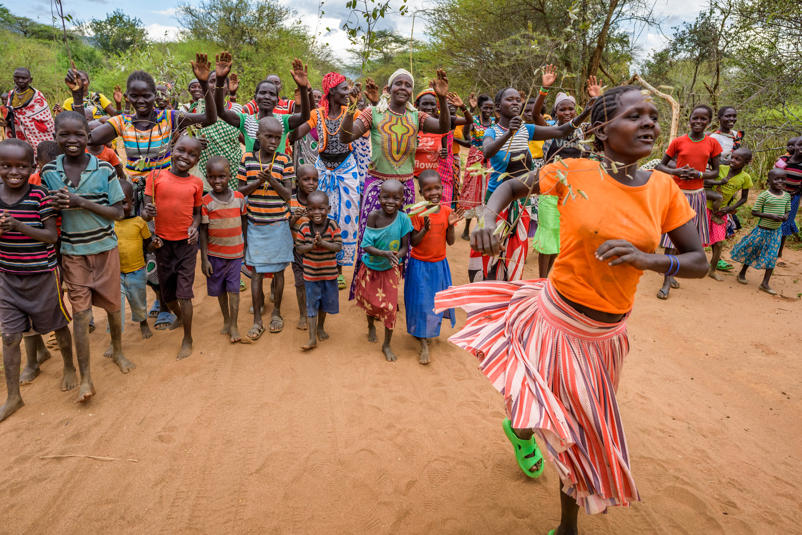 Monica, Cheru’s mother, leads a procession of villagers to the Kesot water kiosk. They’re celebrating the new water system with songs, dances, and games.