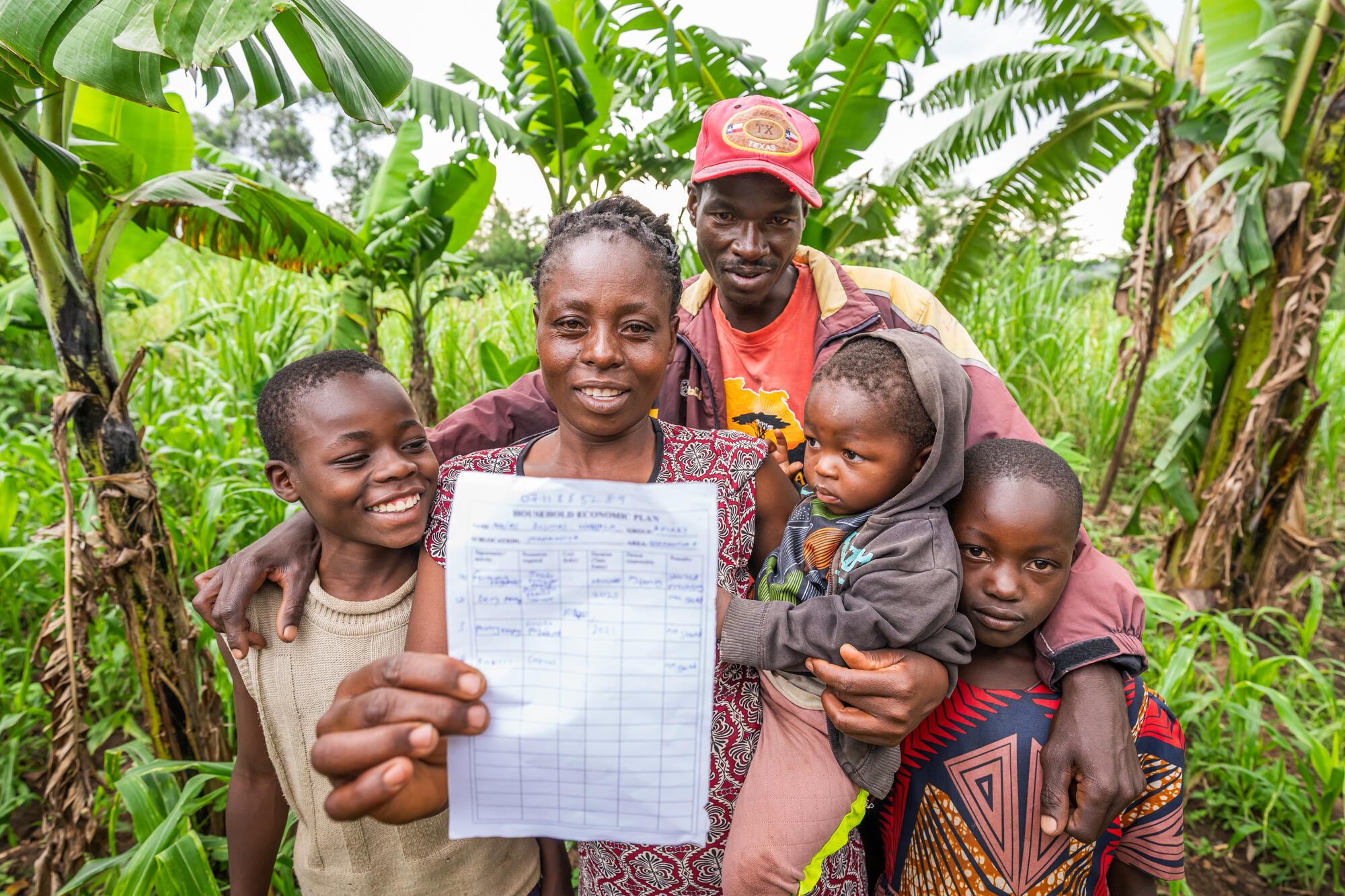 A woman surround by three children and her husband, holds up a piece of paper.