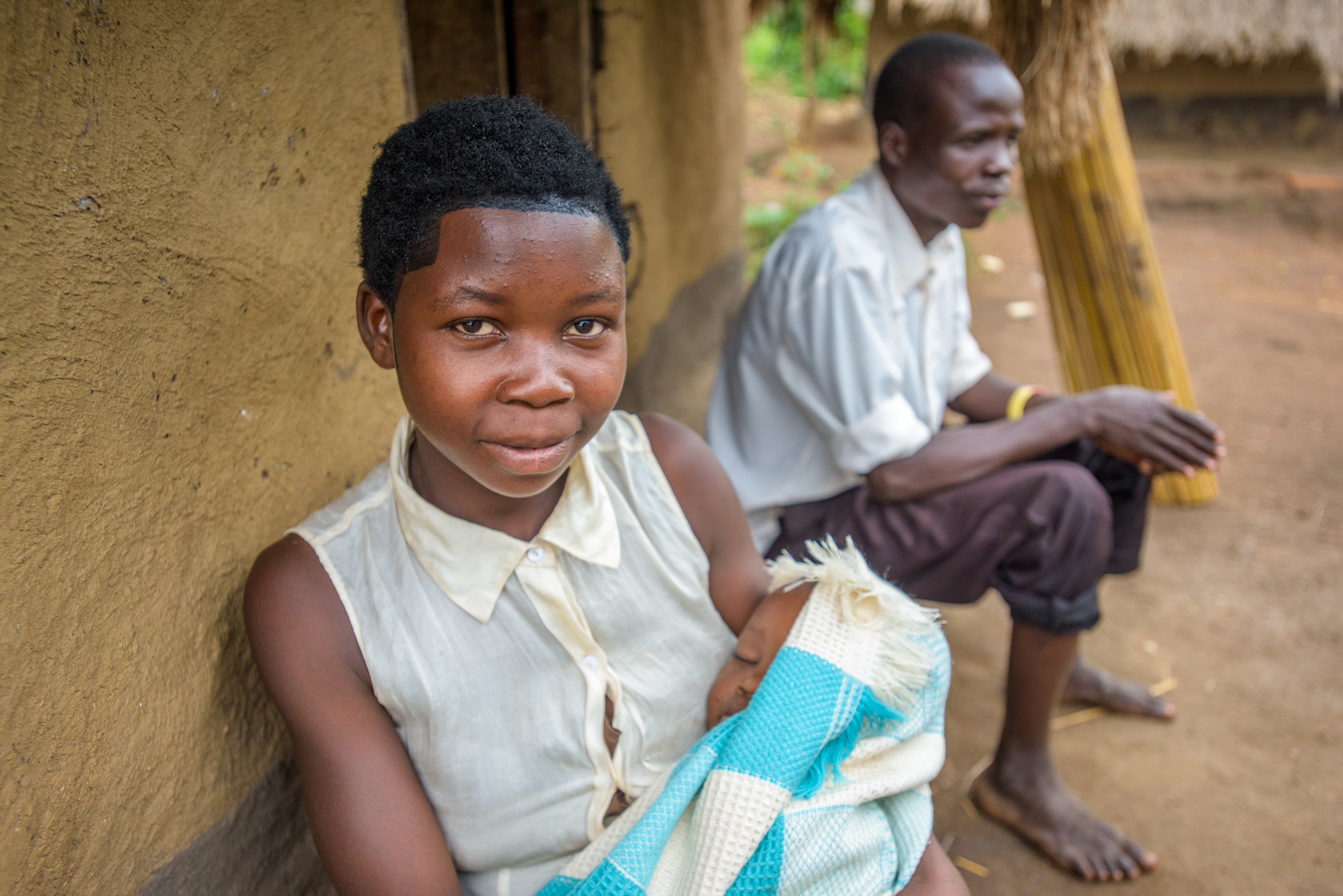 A teen holding her baby with the father in the background