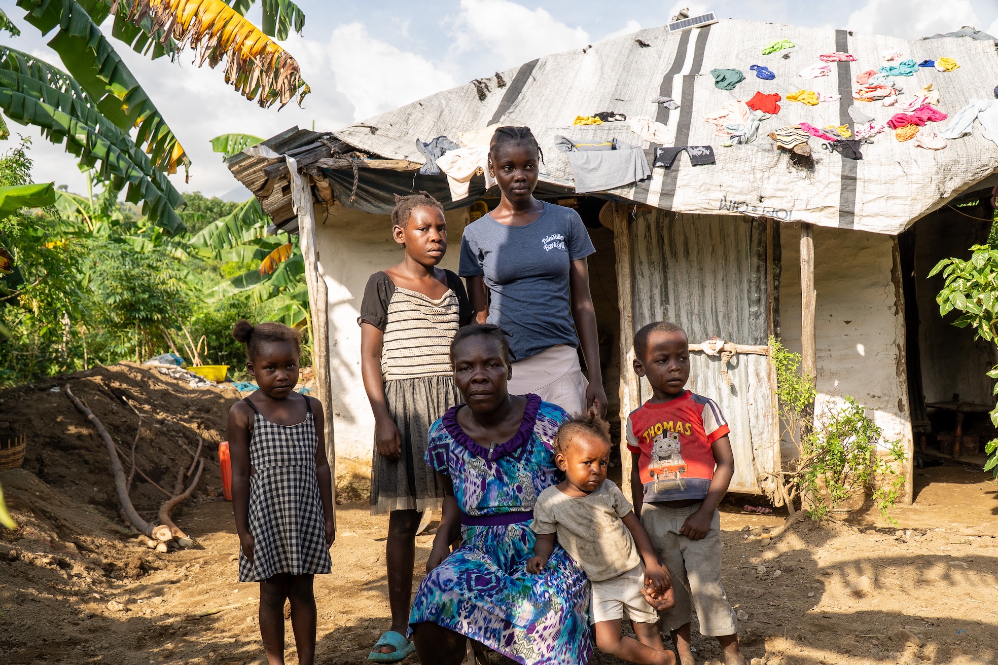 Enize and her children stand in front of their damaged house