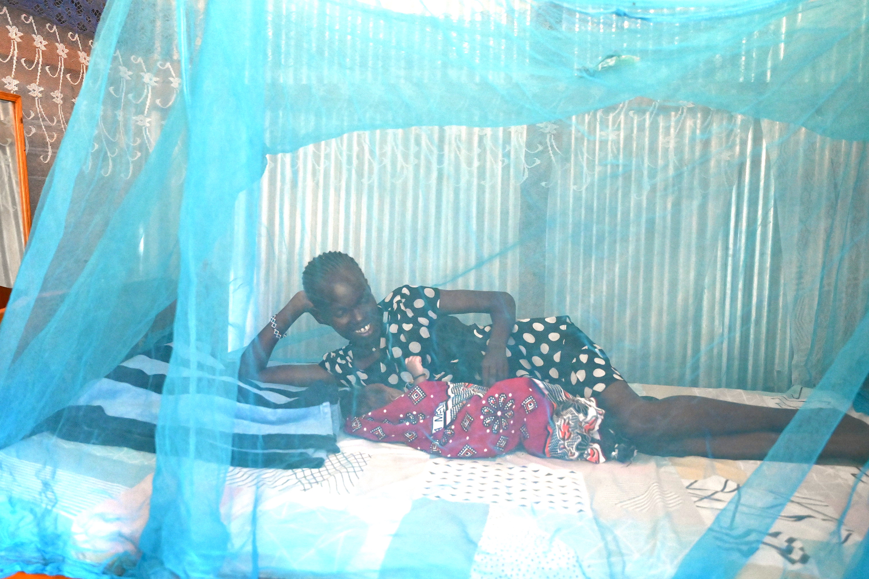 Peris cuddling her under a bed net. ©World Vision Photo/Sarah Ooko.