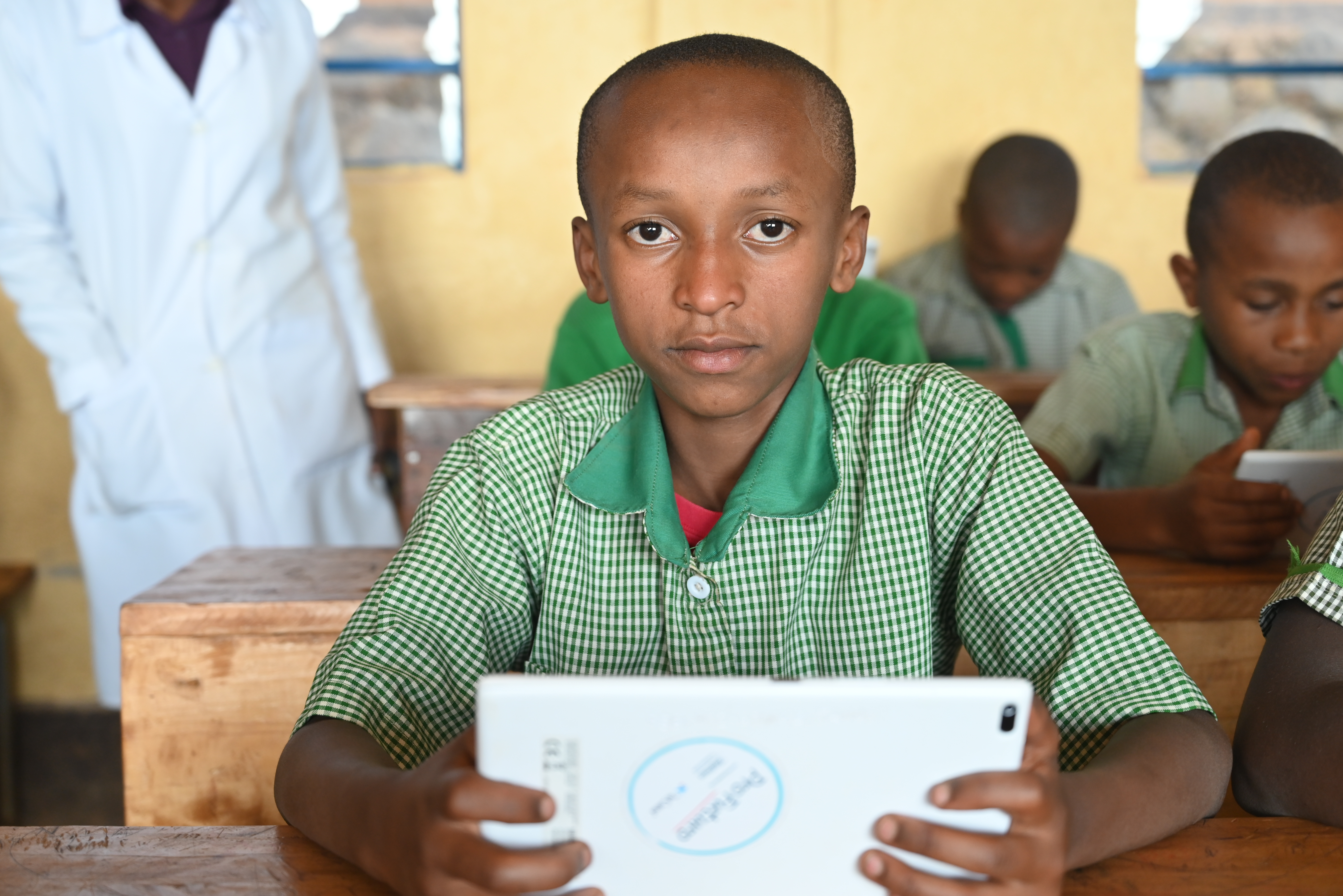Moise in his primary five class holding an ipad he uses for his lessons. The Ipad was provide by ProFuturo project.