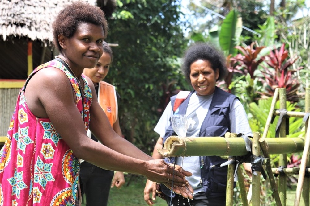 Angela Masit demonstrating how to use a bamboo tippy tap in her plastic compound of Nawaeb District. Angela is behind the mobilisation of her community in reaching ODF status.