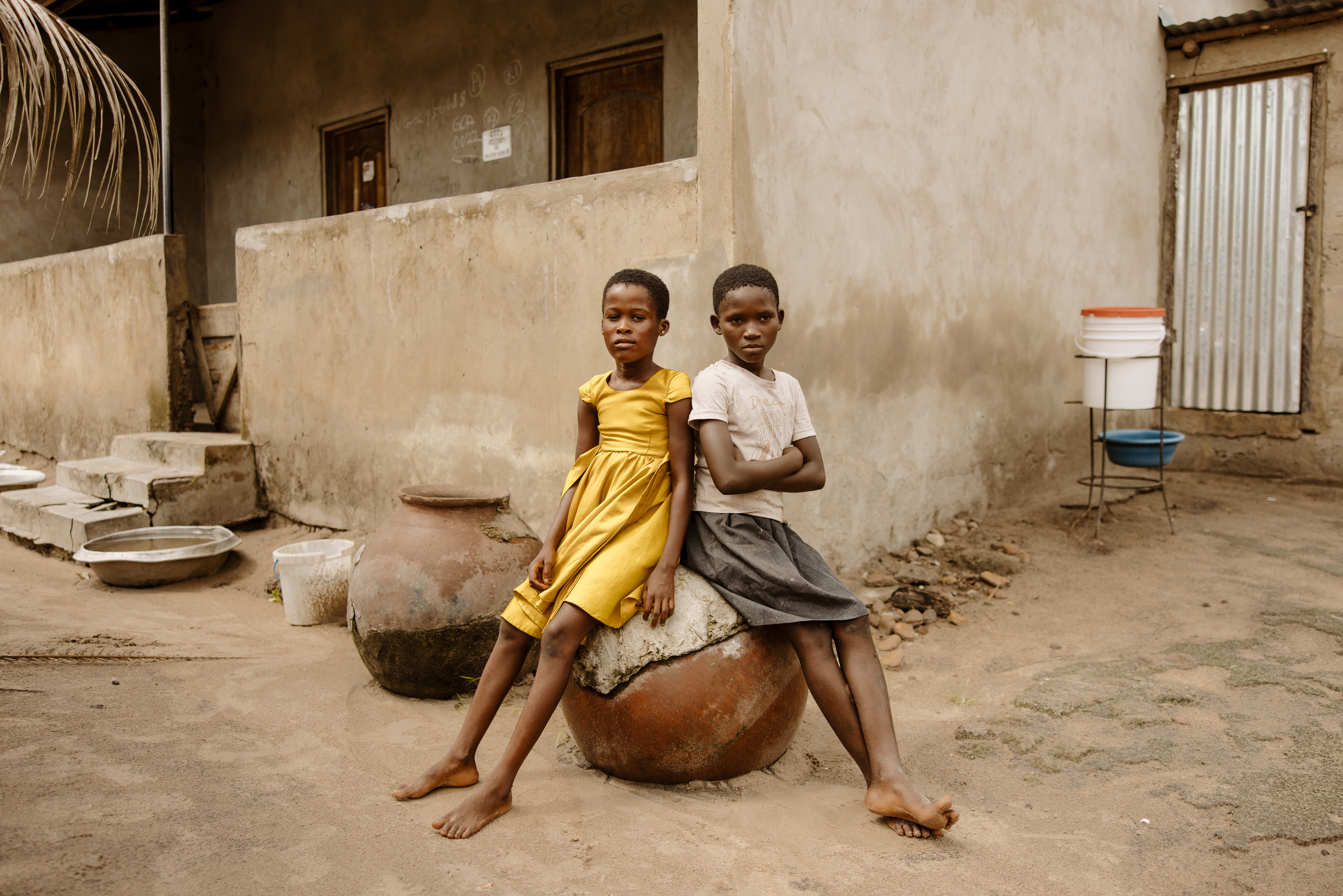 Two girls sit outside a modest home in western Ghana