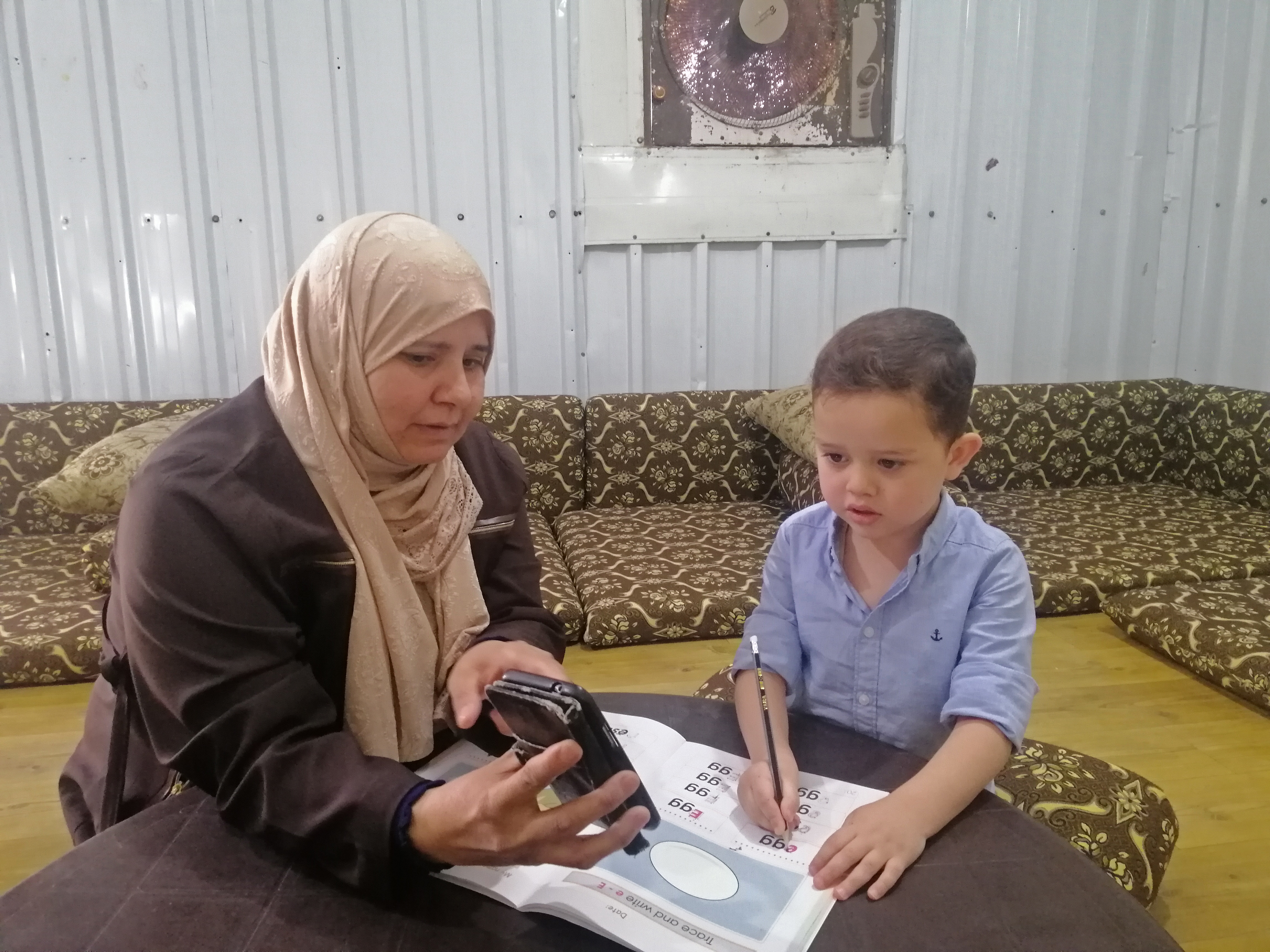 Five-year-old Qutaibah is studying with the help of his mother inside his hom