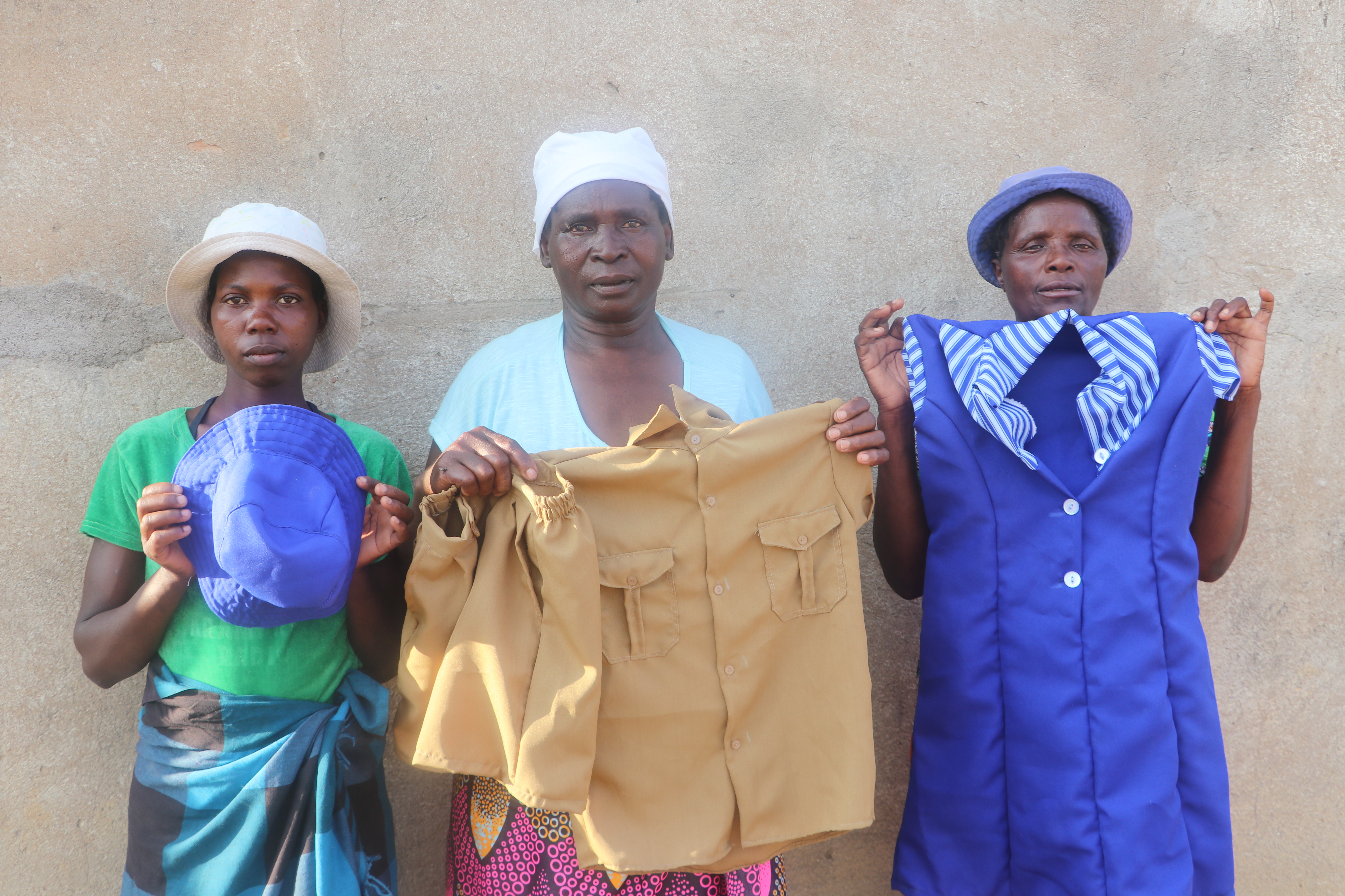 Tendaiishe Group Members holding some of the uniforms they make for children